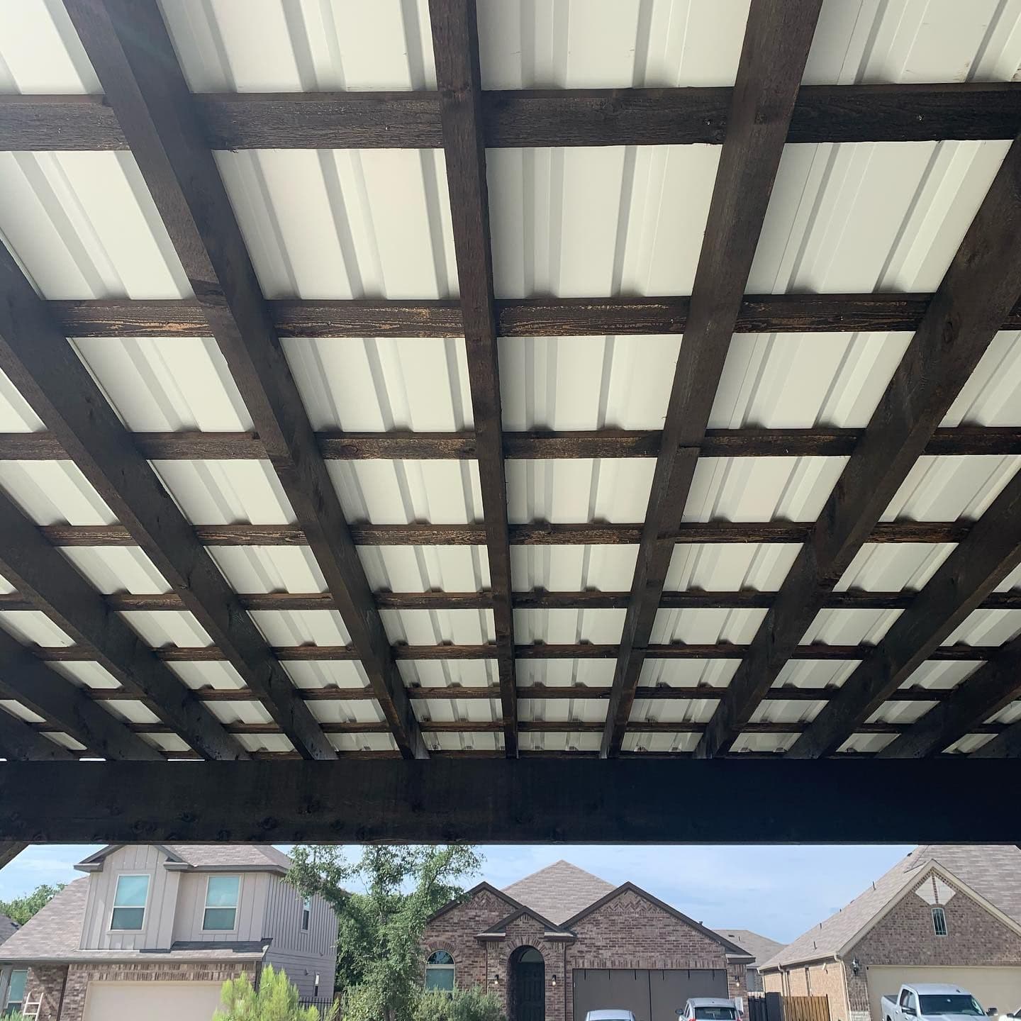 Underside of a dark stained timber patio cover with exposed beams and metal roof panels