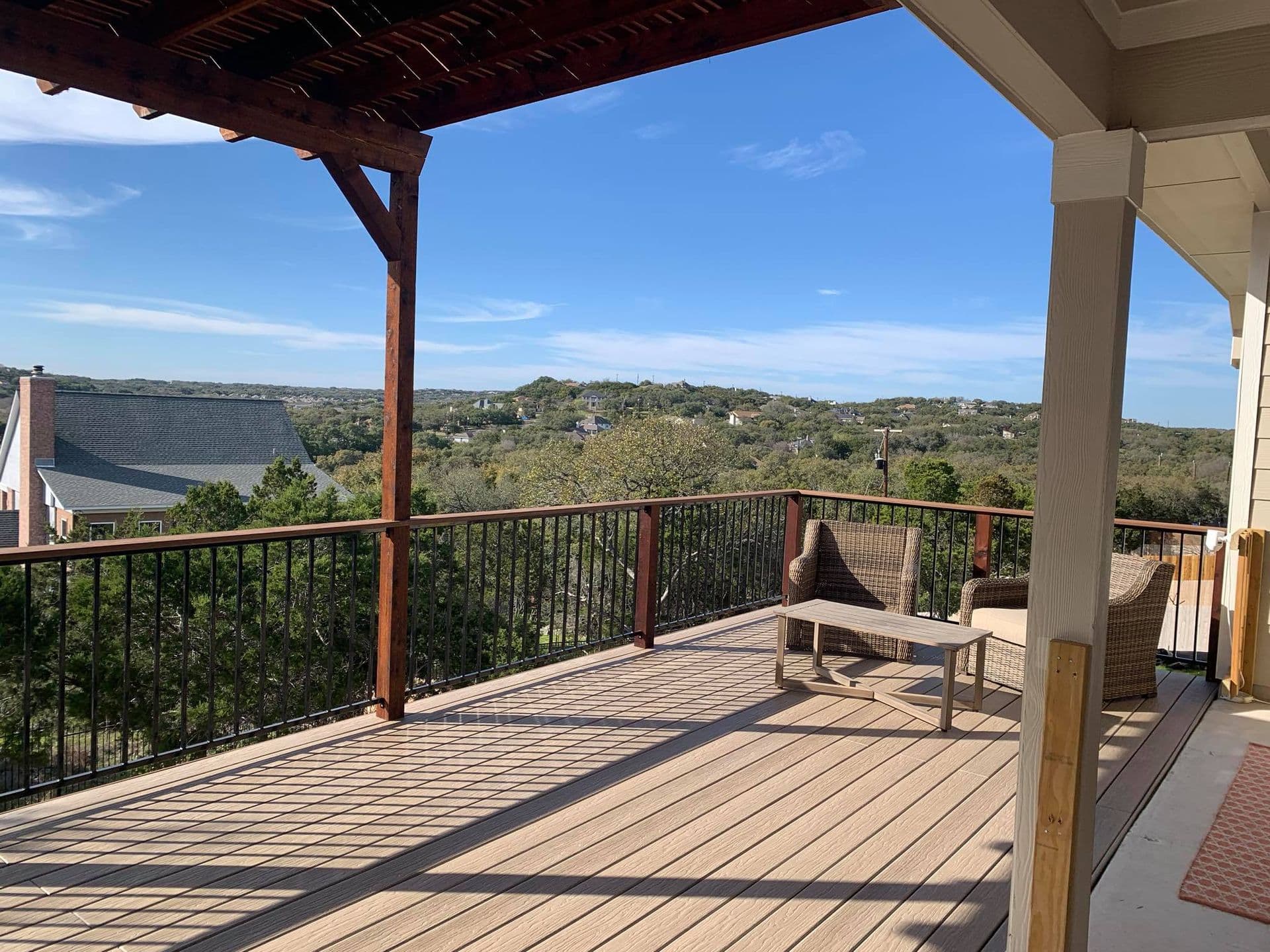 Elevated composite deck with stained pergola beams and metal railing facing a hill country view