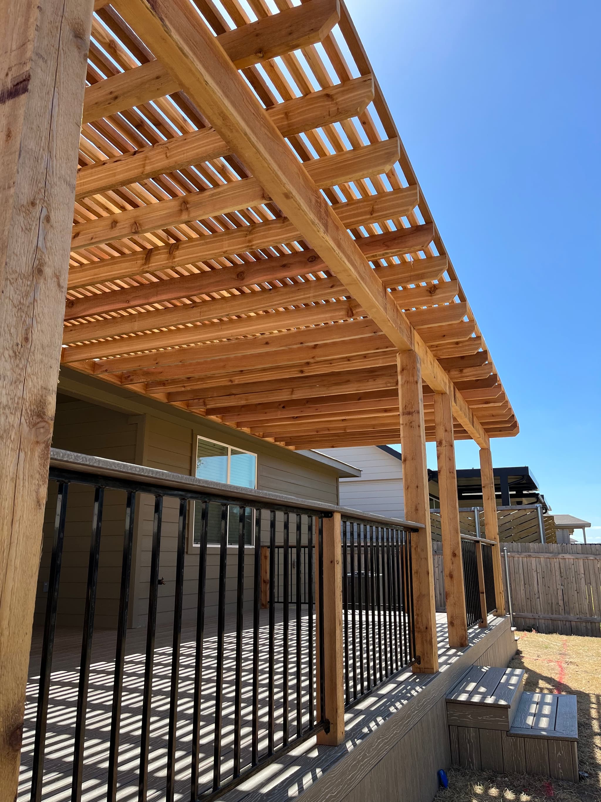 Cedar pergola with tight rafter spacing over a composite deck with black metal balusters