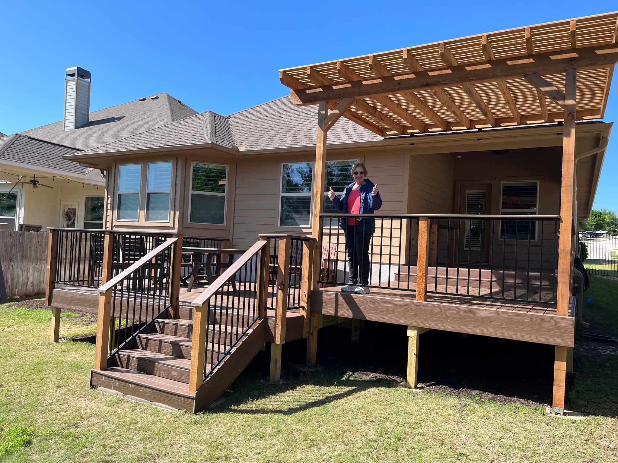 Composite deck with two stair runs, black metal balusters, and a cedar pergola section